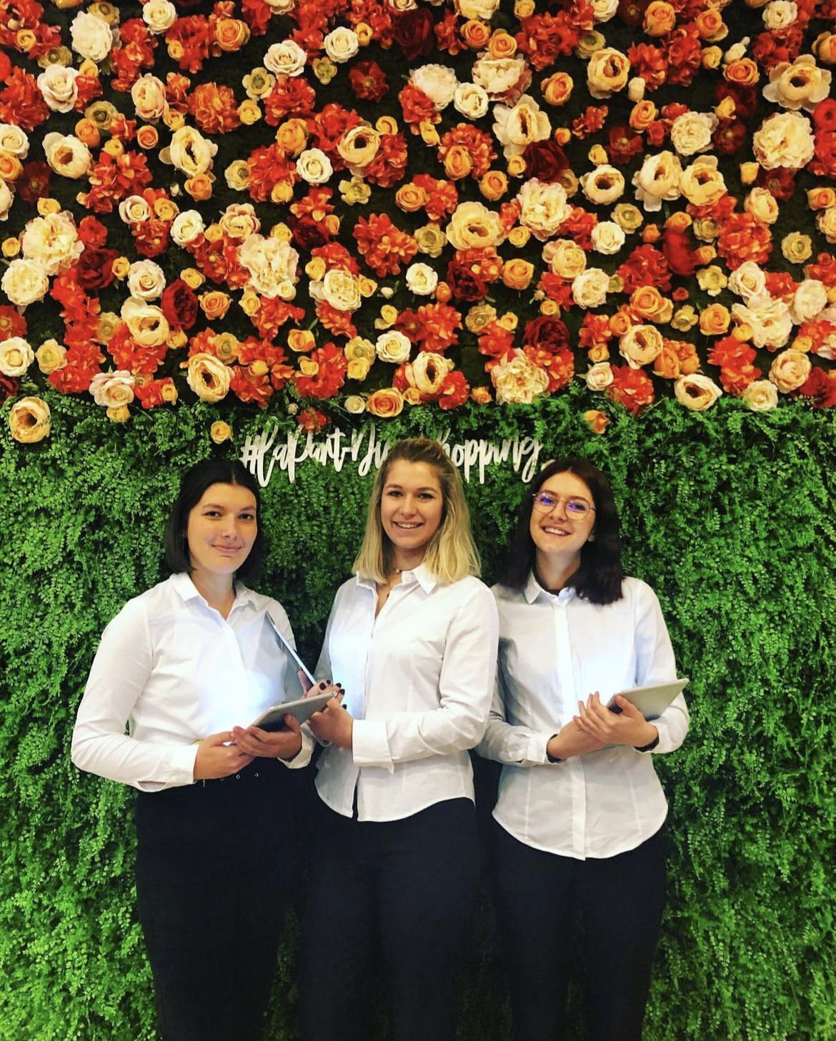 Trois hôtesses devant un mur de fleurs